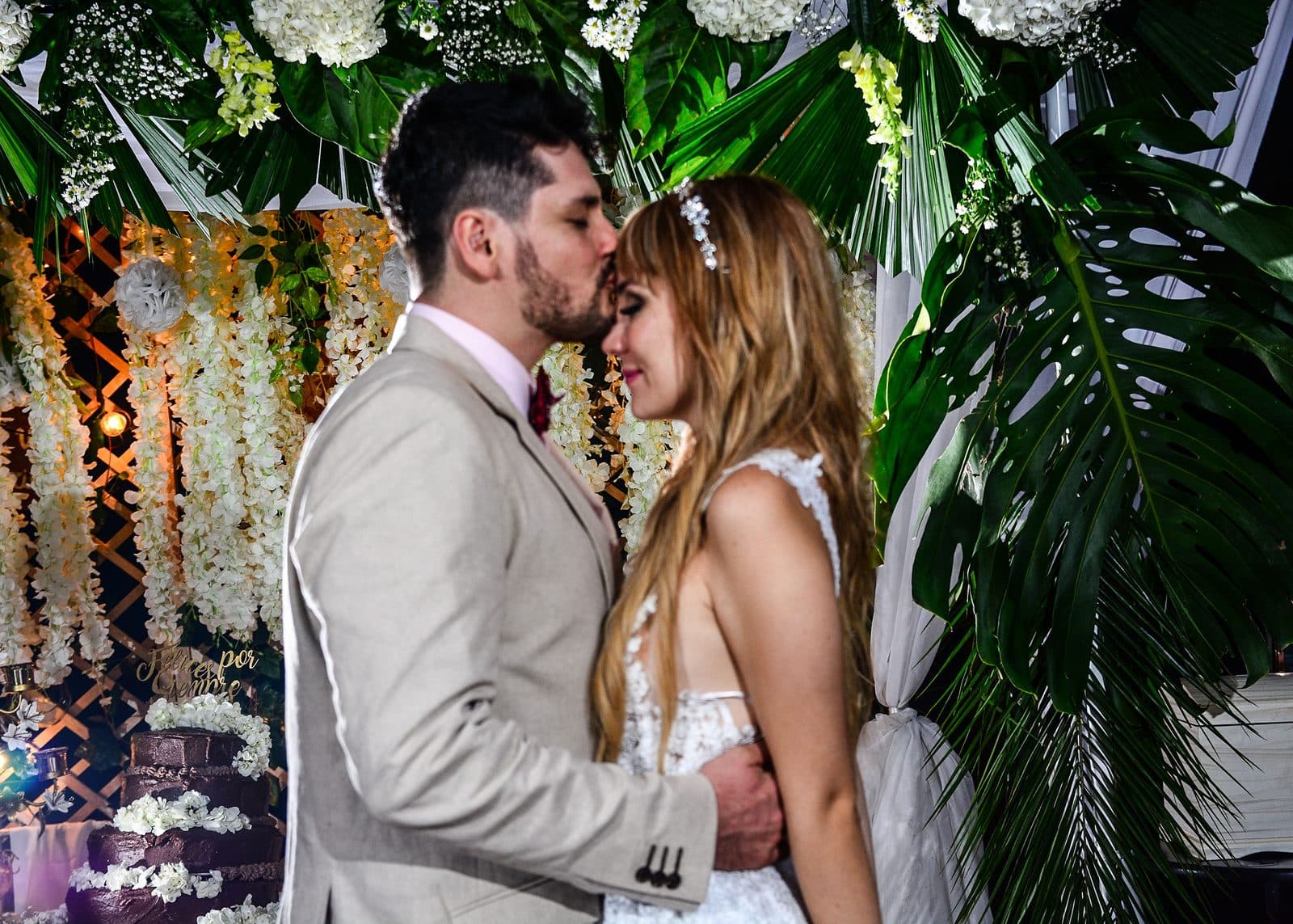 Alejandro kisses Alejandra on the forehead in front of their flower arch