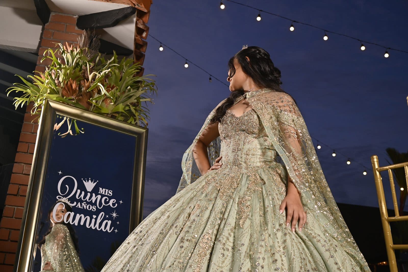 Quinceañera de noche bajo una guirnalda de luces, con vista a las montañas